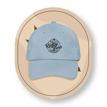 A light blue rugby cap with a black embroidered 'Rugby Brew Coffee Co' logo on the front, presented on a beige circular graphic background.
