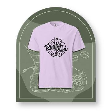 A light lavender crewneck rugby t-shirt with a black circular 'Rigby Brew Coffee Co' graphic on the chest, presented on a stylized dark olive green arched background with coffee-themed line drawings.